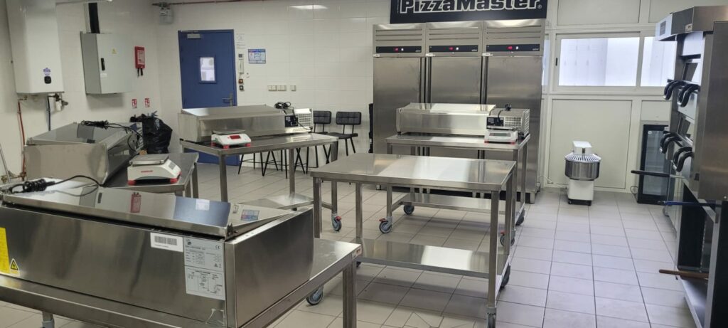 Photographie d'une cuisine professionnelle illustrant le principe de la marche en avant avec des zones sales et propres délimitées au sol par des flèches. Un chef travaille à une station de préparation propre, et une tablette au premier plan affiche le logo OAFormation avec une checklist d'audit de cuisine, soulignant l'importance de la réglementation et de l'ergonomie