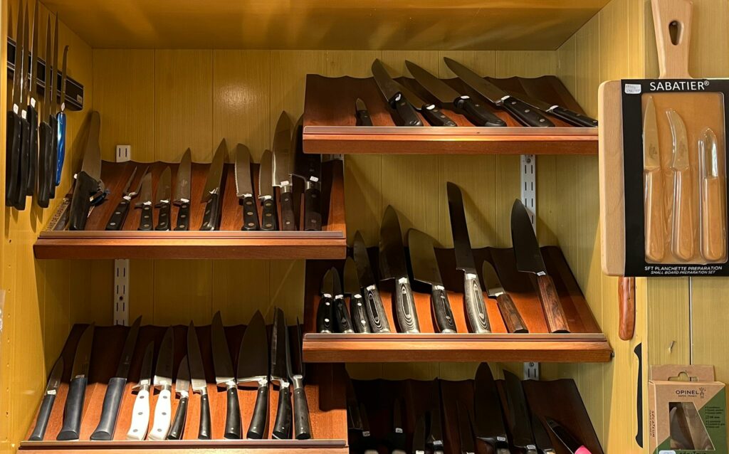 Présentoir en bois exposant une large sélection de couteaux de cuisine professionnels dans une coutellerie, avec différents modèles japonais et européens soigneusement alignés.